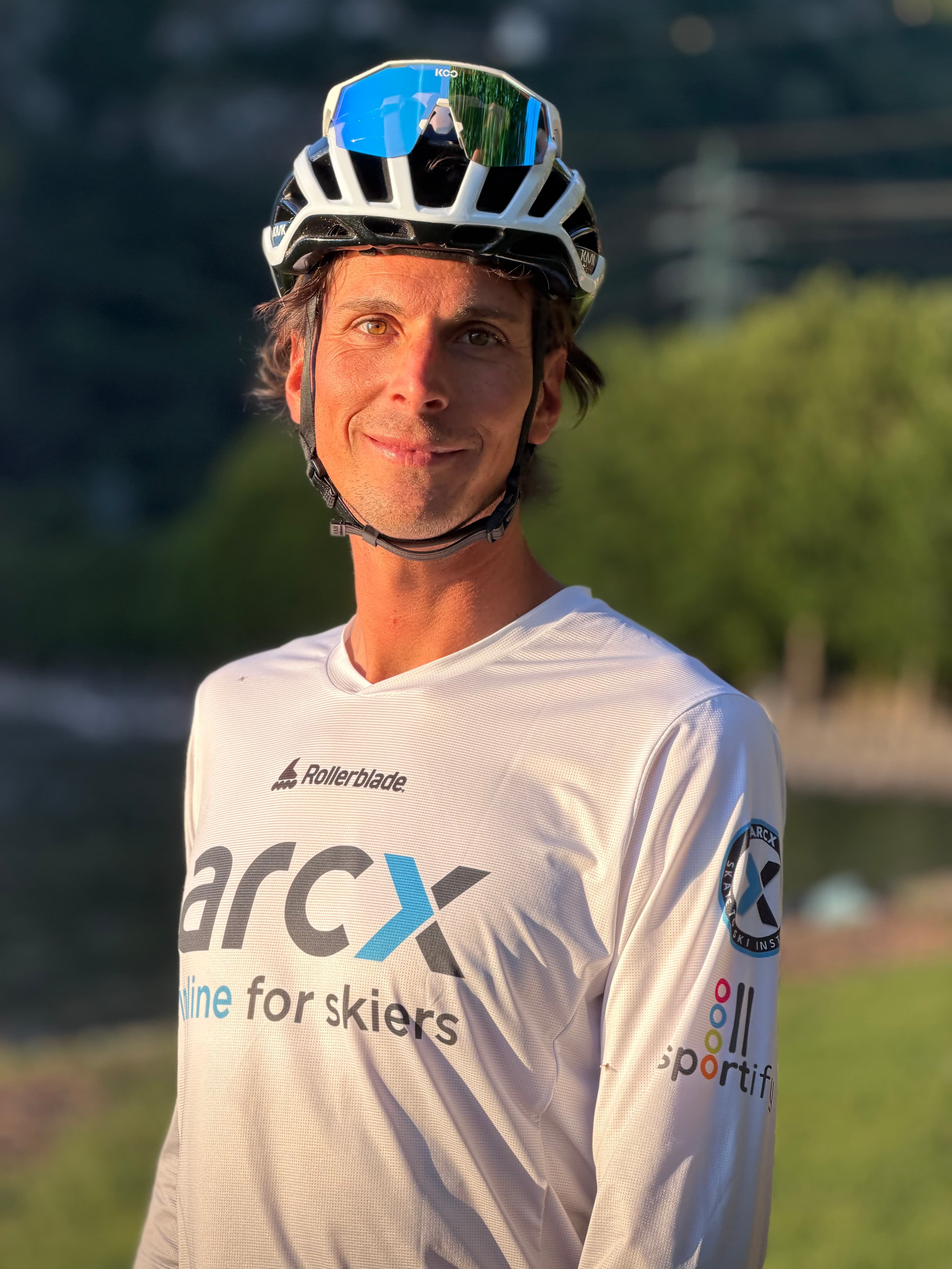 Uomo sorridente con casco bianco e maglia tecnica bianca all'aperto sotto la luce dorata.