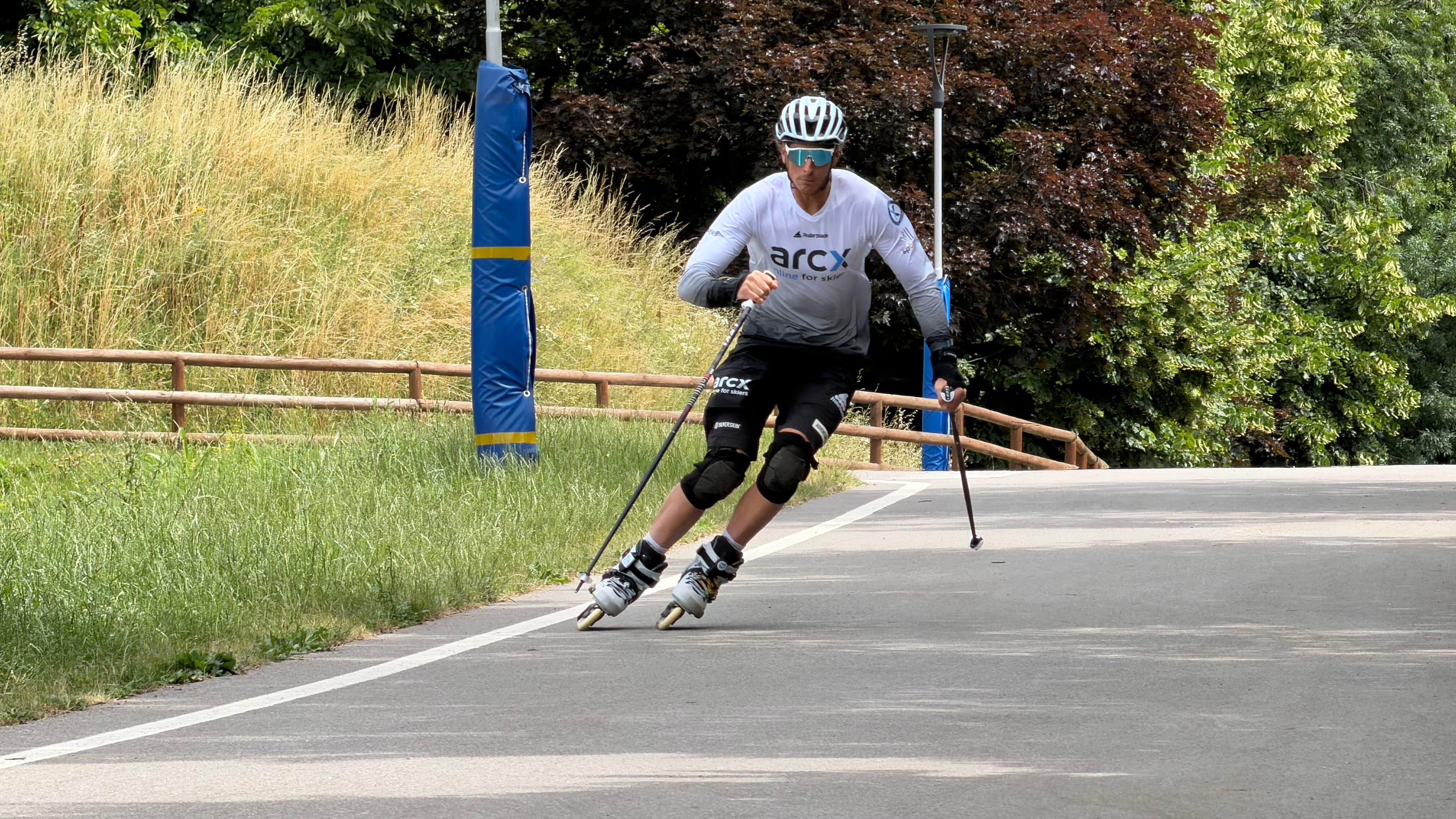Uomo con casco e bastoncini che pratica pattinaggio in linea su una pista nel parco.