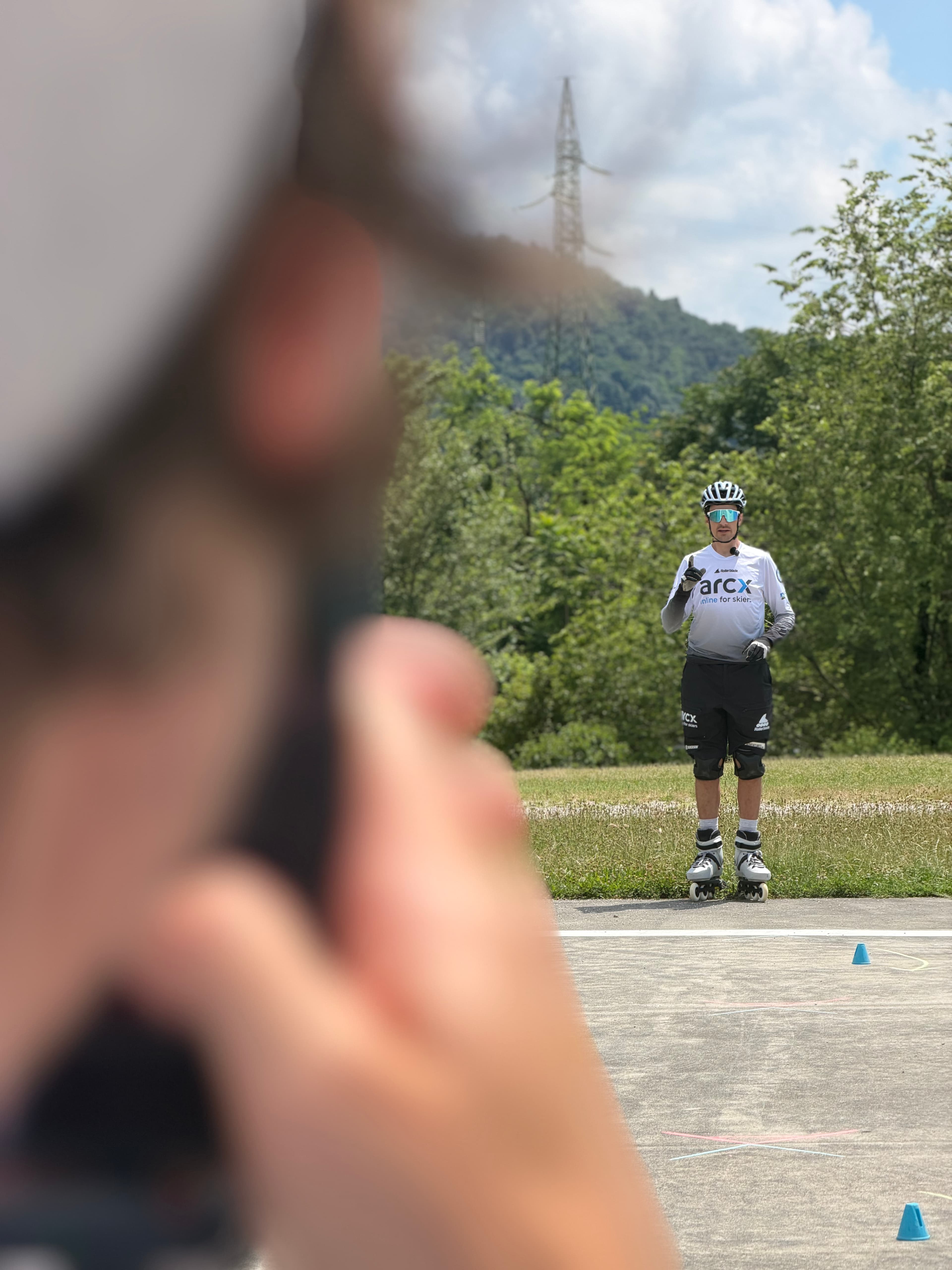 Pattinatore in linea con casco e maglia bianca gesticola su una pista asfaltata all'aperto.