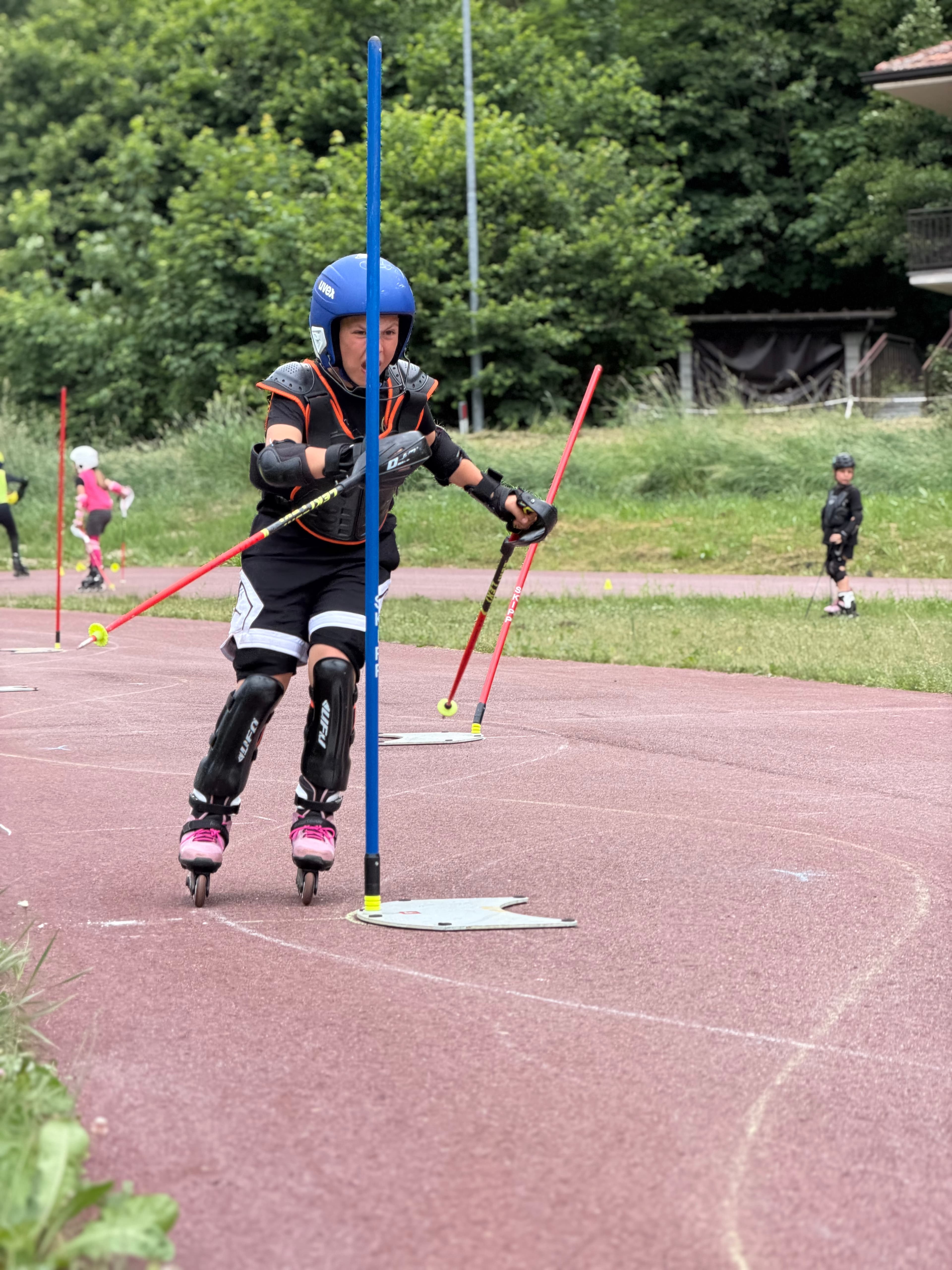 Bambino con protezioni complete fa slalom su pattini in linea tra pali blu e rossi.